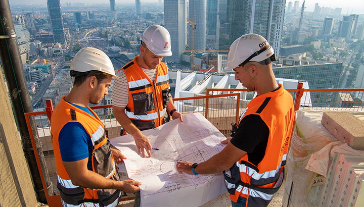 3 מהנדסים עומדים על גג בניין ובוחנים תכנית מתאר